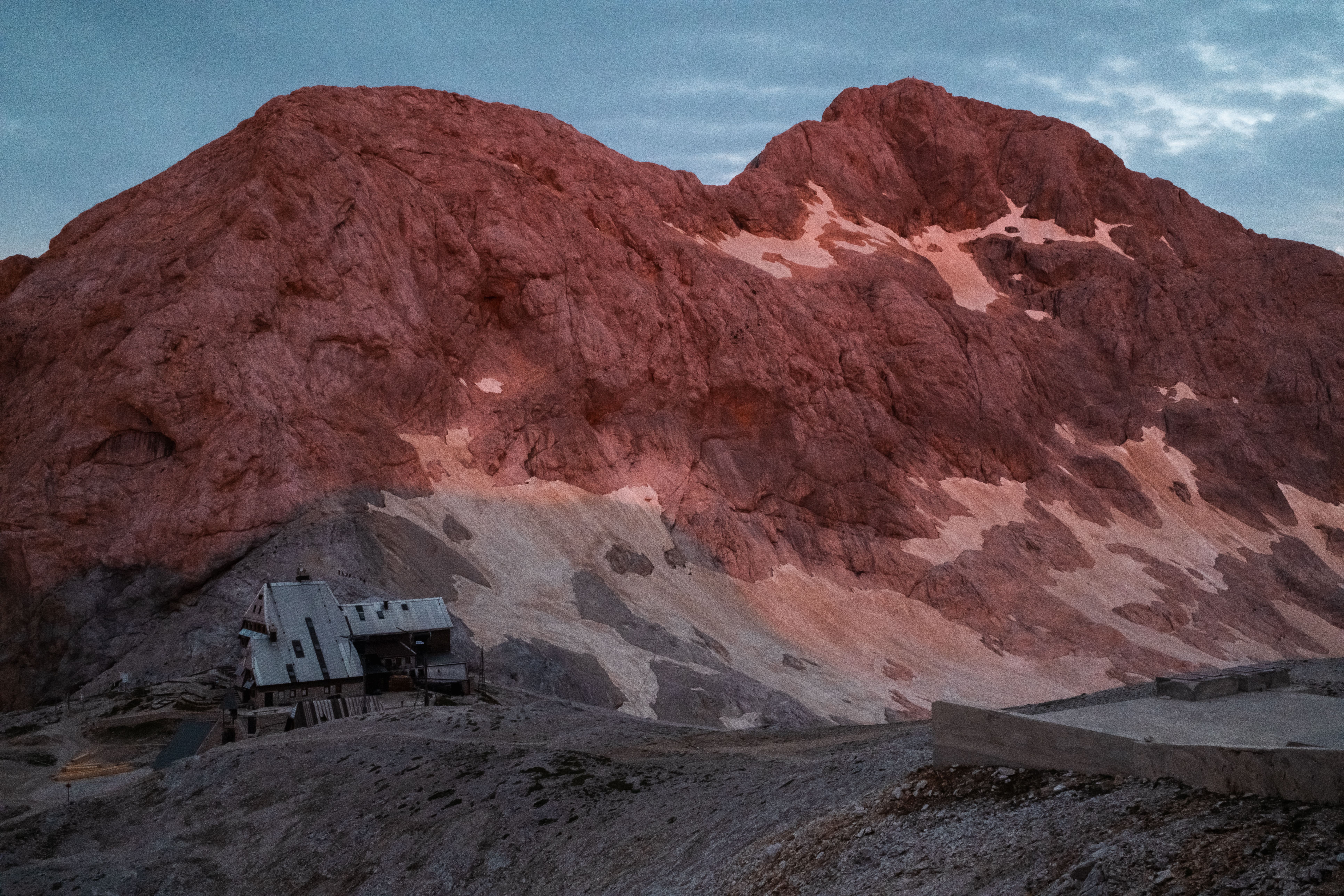 Majestic pink-hued mountain with a rustic cabin below during sunrise in Slovenia's Julian Alps.