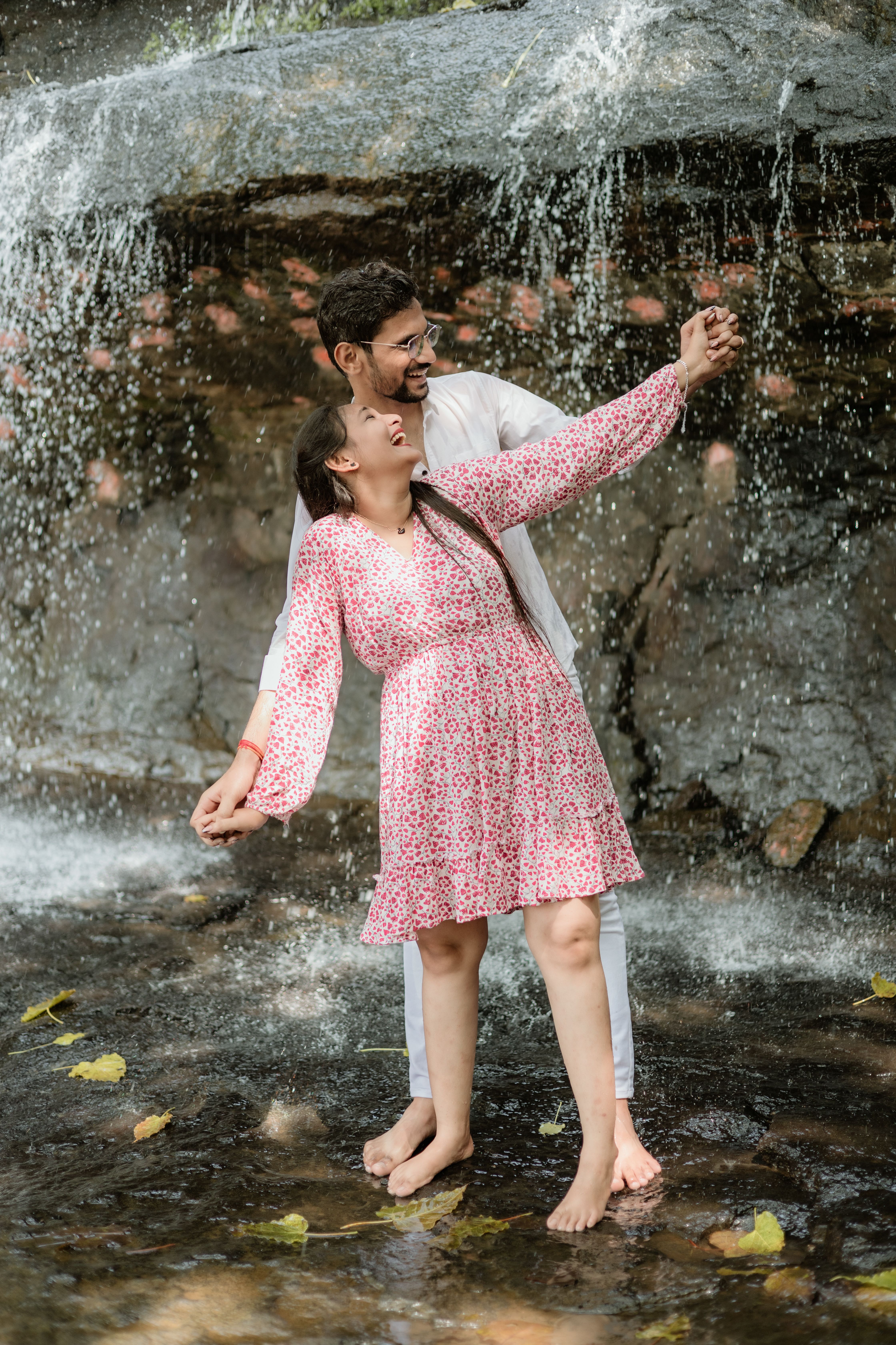 A happy couple enjoys a playful dance by a waterfall, capturing joy and romance in nature. - Fotografer Sidoarjo