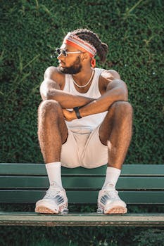 Fashionable adult man in casual attire sitting on a bench, soaking up the sun.