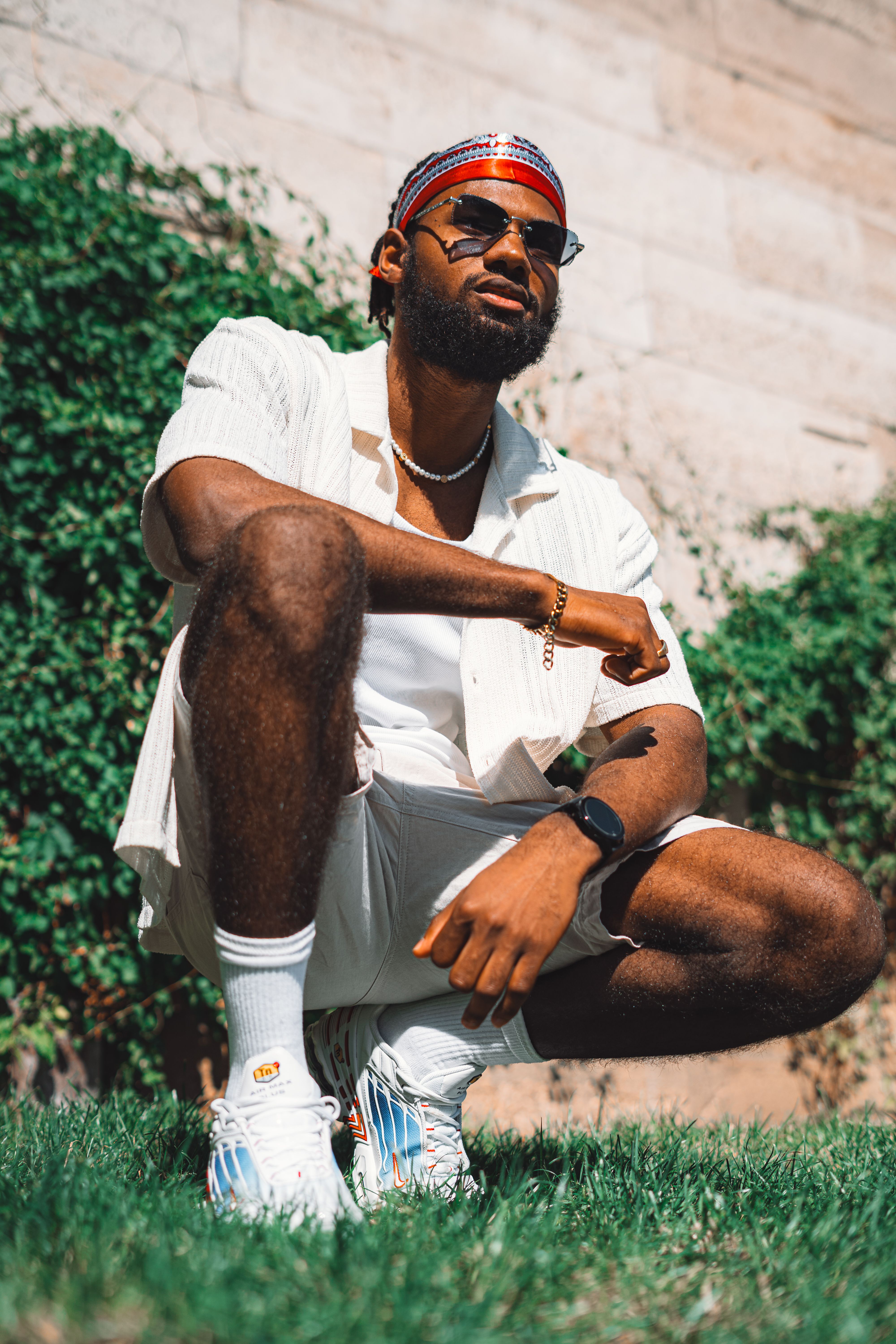 A fashionable man in sunglasses and headband posing confidently in a sunny outdoor setting.
