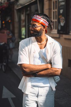 Portrait of a stylish man with a headband, sunglasses, and facial hair on a sunny urban street.
