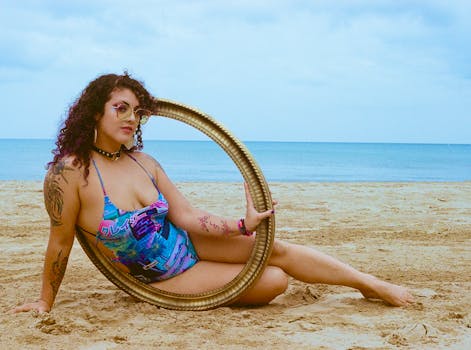 A woman in a swimsuit holding a frame poses on a beach, surrounded by sand and sea.
