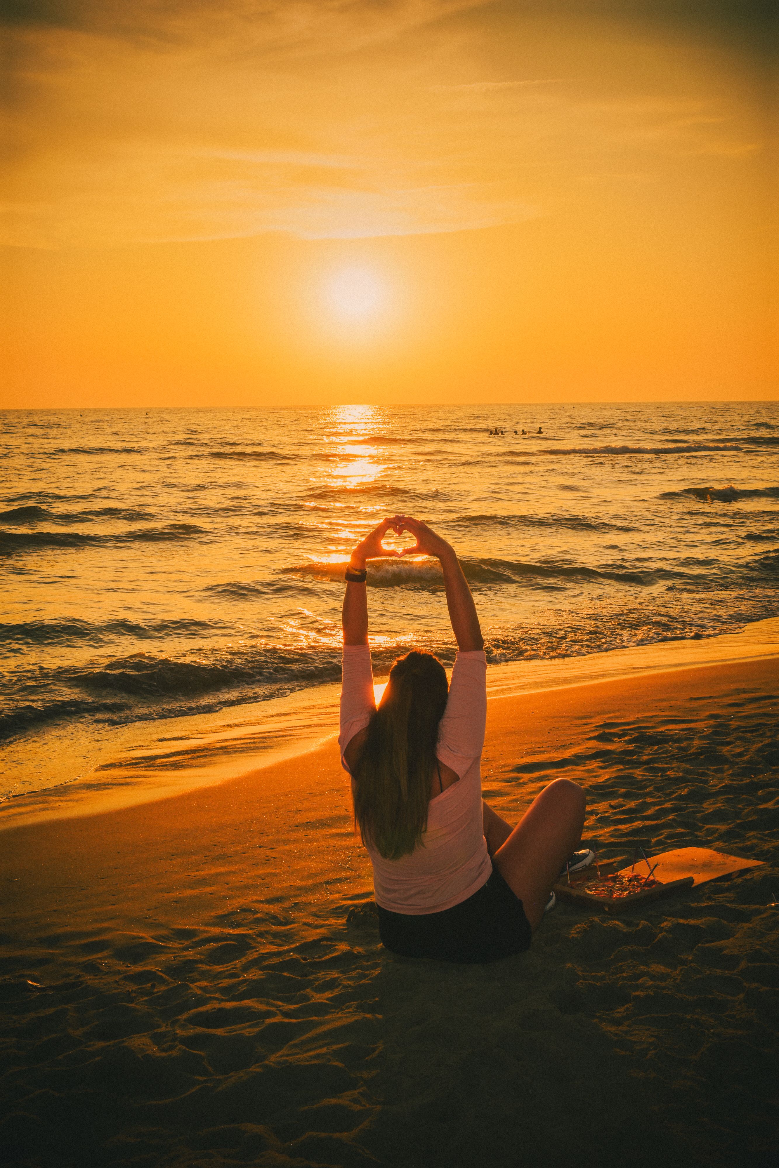 A woman sitting on the beach with her hands in the air · Free Stock Photo