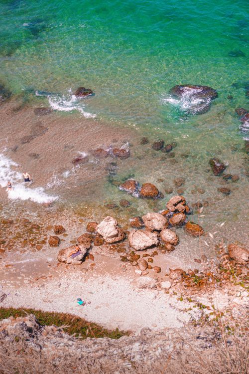 Free Aerial view of a serene rocky beach with clear turquoise waters, perfect for a tranquil escape. Stock Photo