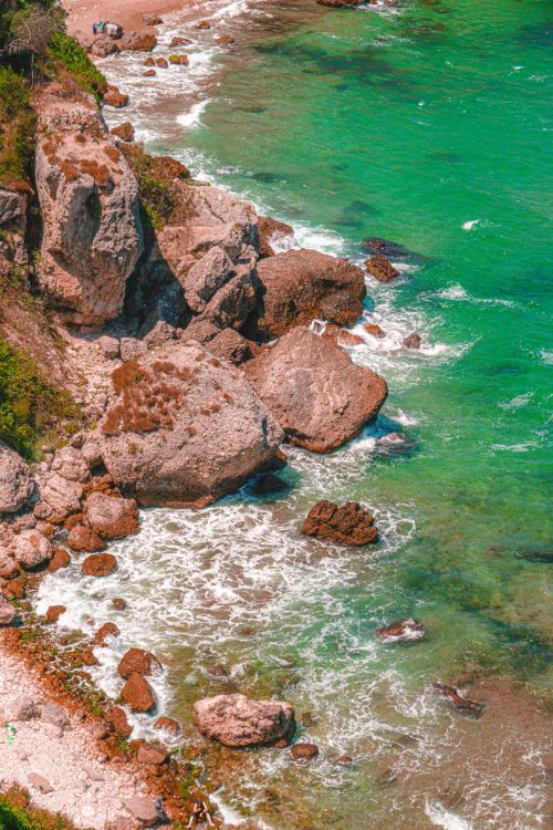 Free Aerial view of rocky coastline with turquoise ocean waves, ideal for travel and nature themes. Stock Photo