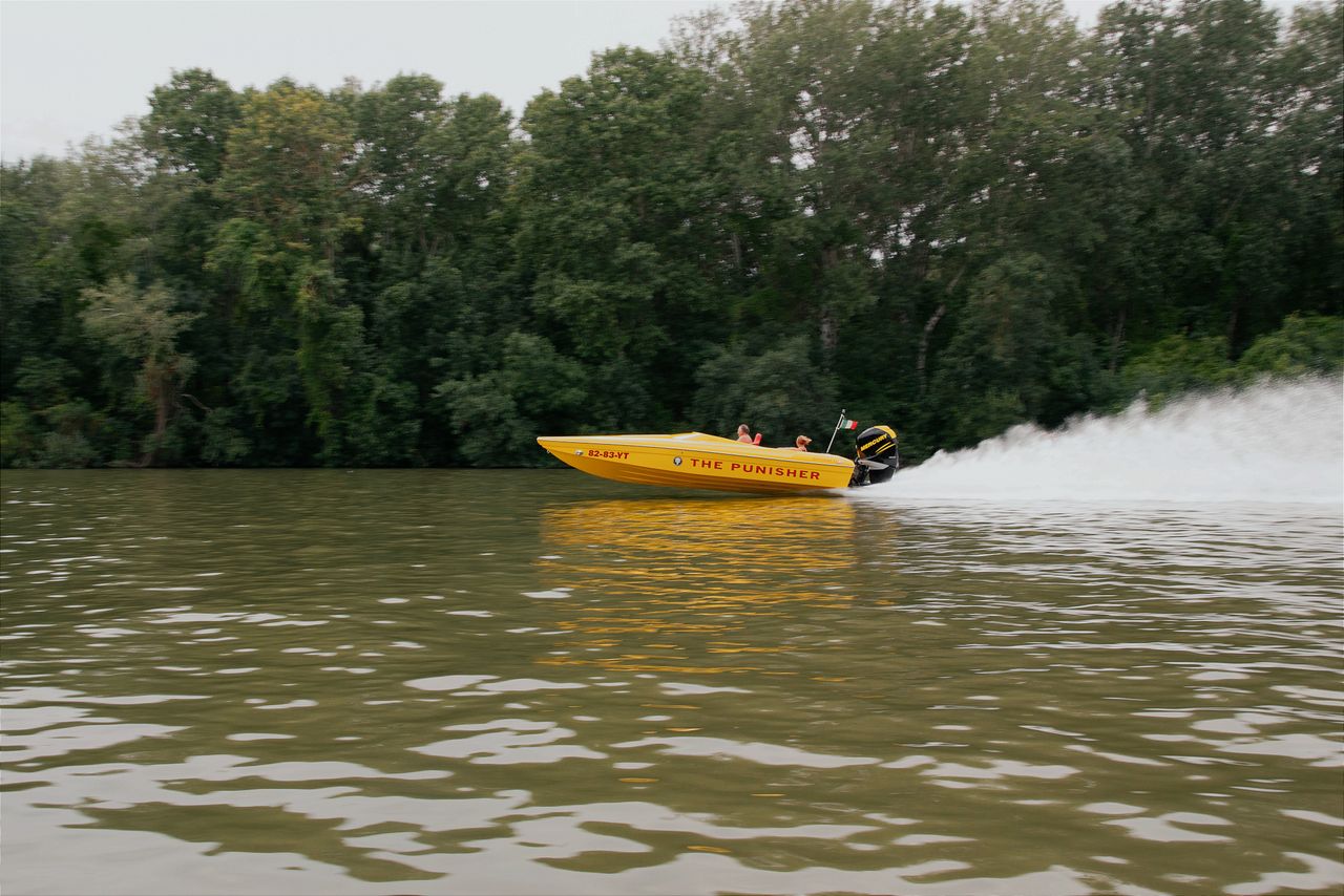a vibrant yellow speedboat racing on a serene hungarian river with lus