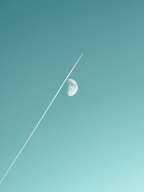 A stunning view of an airplane contrail intersecting with the crescent moon on a clear day.