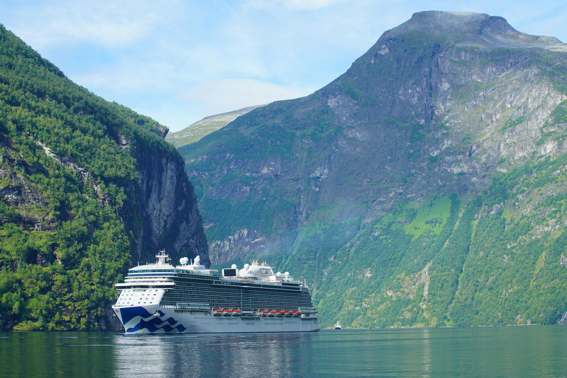 Explore the majestic Geiranger Fjord in Norway with a luxurious cruise ship surrounded by towering mountains.