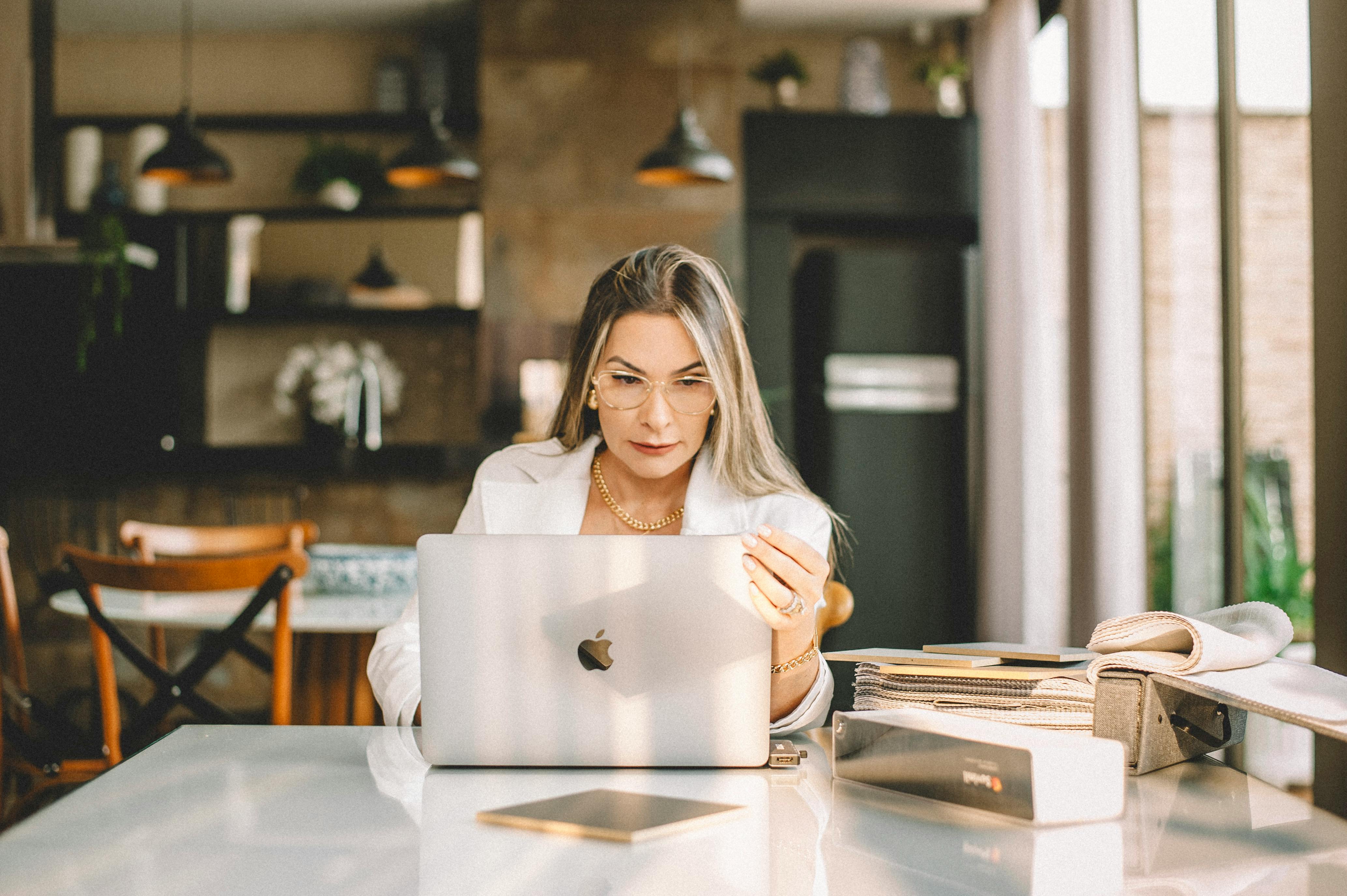 blonde woman sitting at table with apple macbook in kitchen