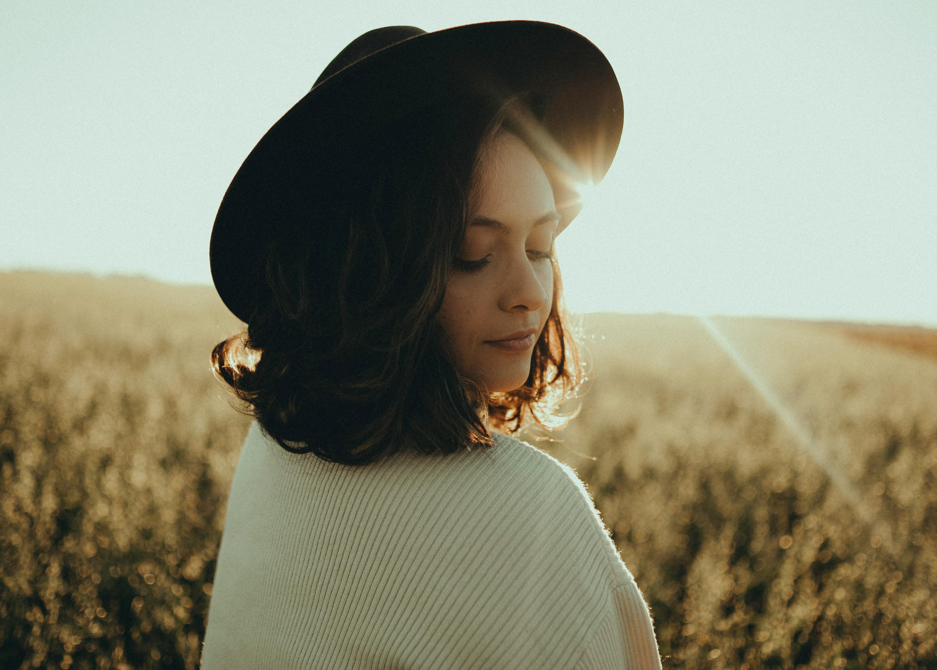 Serenely backlit portrait of a woman in a sunlit field wearing a hat.
