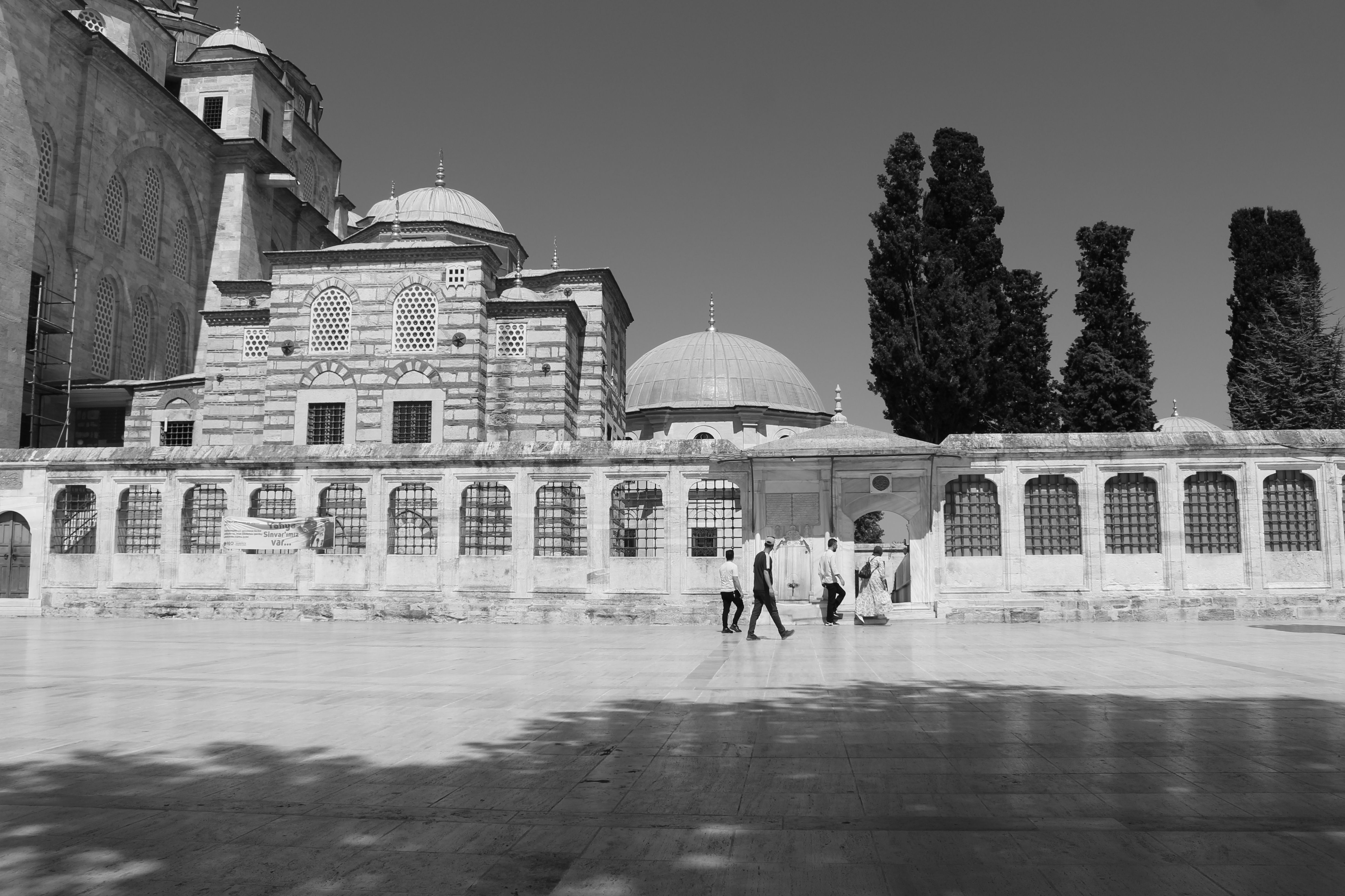 Black and white photo of a historic Ottoman mosque with domes and people walking in Istanbul.