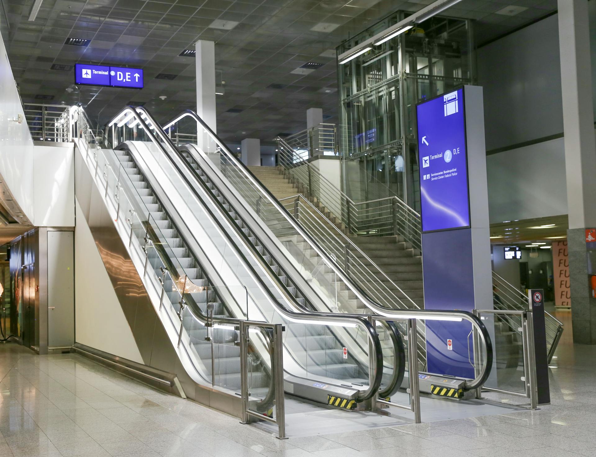 Contemporary airport terminal with empty escalator and clear signage indicating direction.