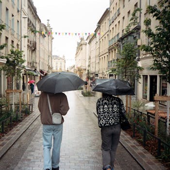 Two people with umbrellas walking in rainy Nancy, France's charming streets.