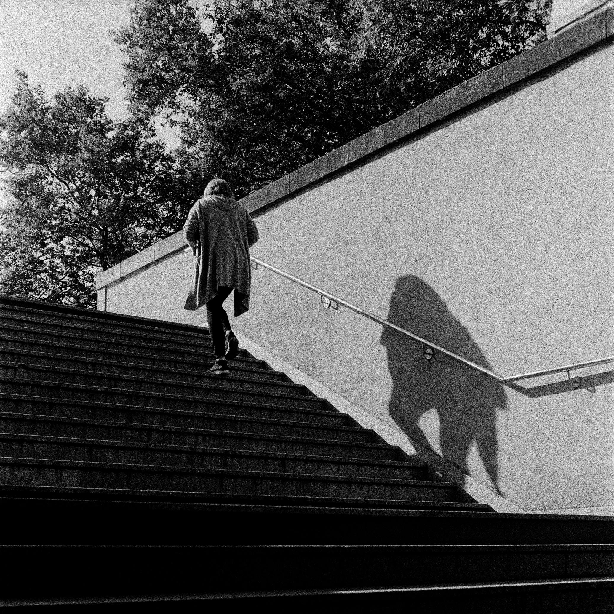 Black and white photo of a person walking up stairs, casting a shadow in Metz, France.