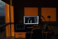 在灯光昏暗的家庭办公室里，桌面和笔记本电脑被橙色的日落灯光照亮