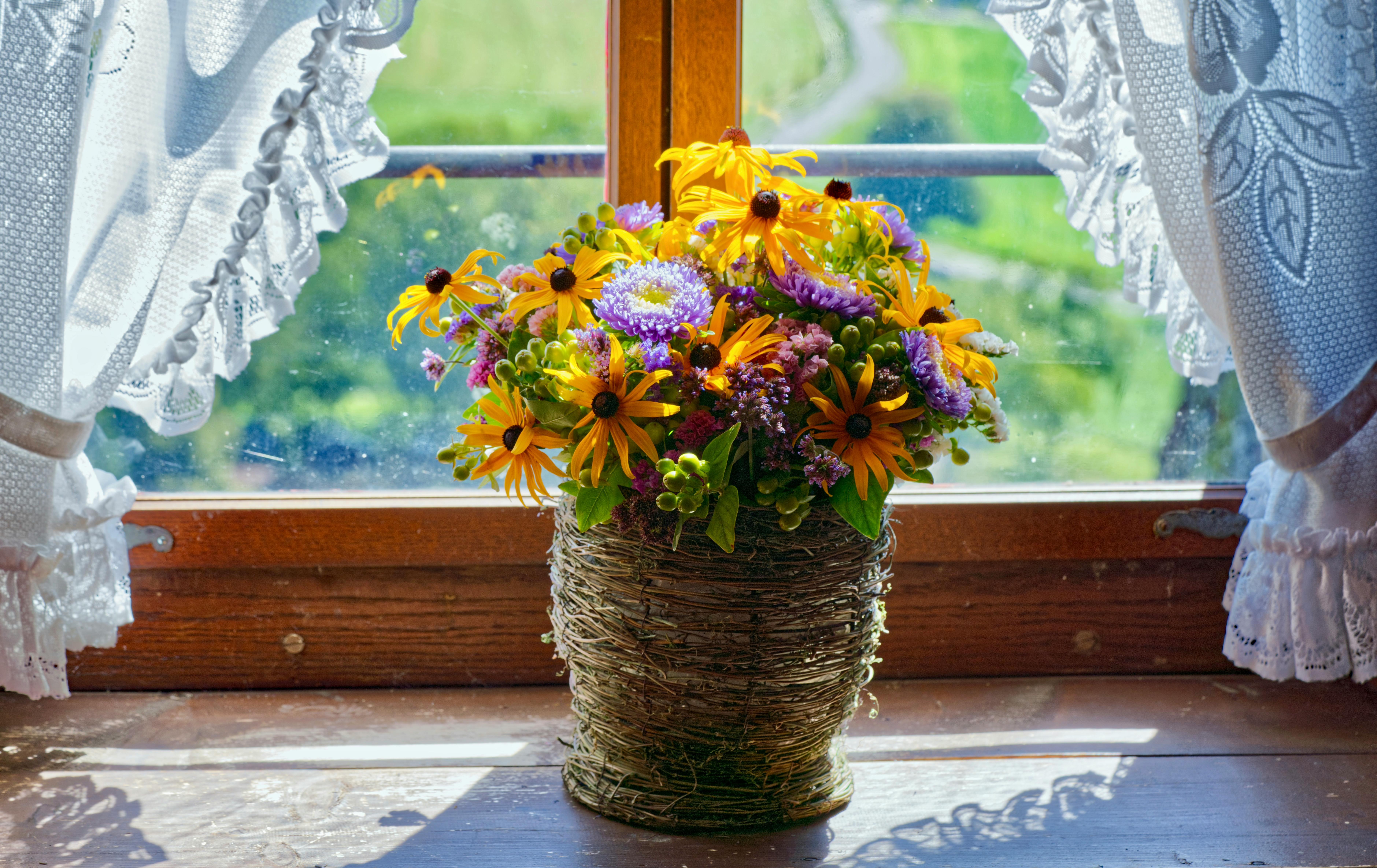 A vibrant bouquet of summer flowers in a wicker basket by a sunny window.