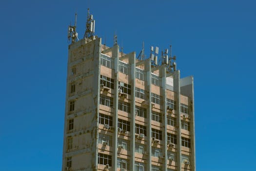 A tall urban building with antennas and a weathered exterior under a clear blue sky.