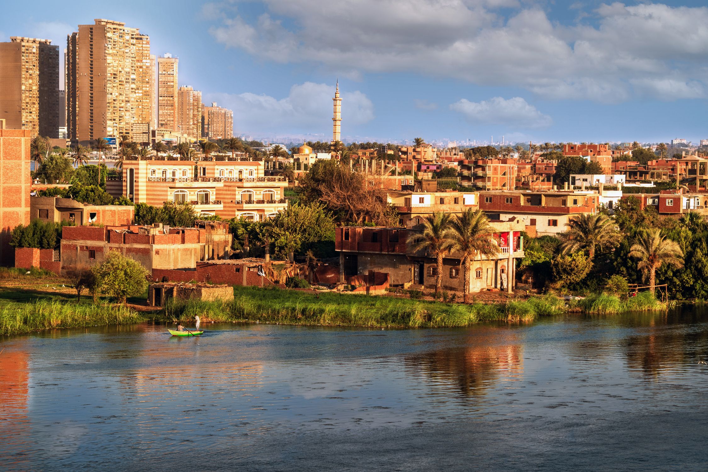 Urban and rural landscape with river, buildings, and a mosque in the background.