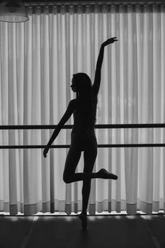 Silhouette of a graceful ballet dancer practicing in an indoor studio, highlighting art and strength.