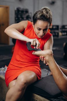 A professional therapist in a red dress provides foot therapy to a client at a gym, enhancing wellness and relaxation.