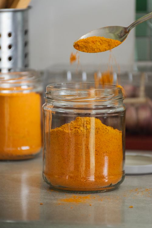 Free Rustic kitchen scene with turmeric powder being poured into a glass jar. Perfect for seasoning or cooking concepts. Stock Photo