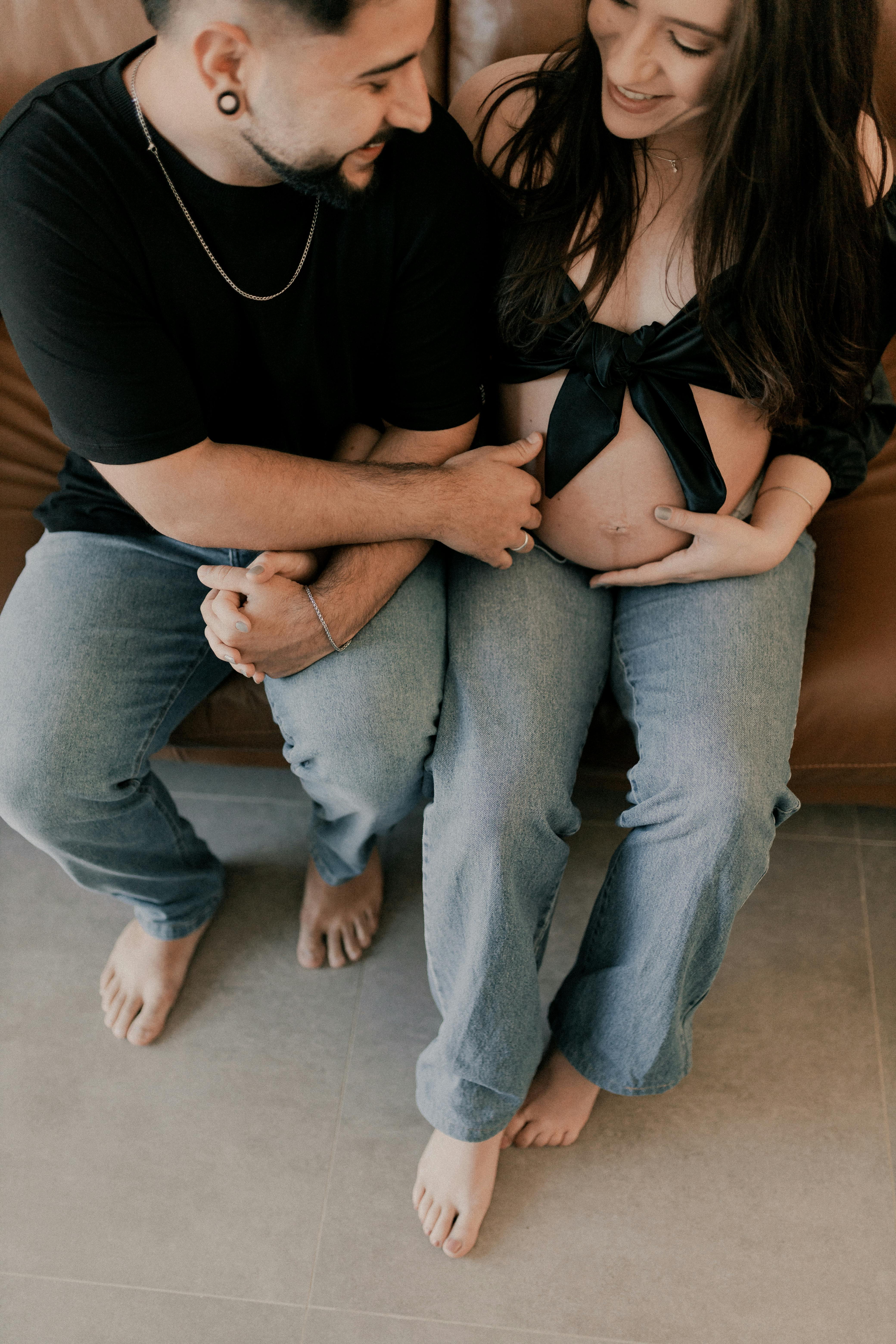 A loving couple embraces on a sofa, celebrating pregnancy with joy and affection.