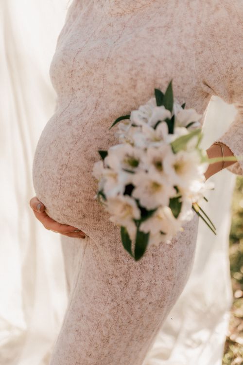 Free A pregnant woman gently holds a bouquet of white flowers, symbolizing new beginnings. Stock Photo