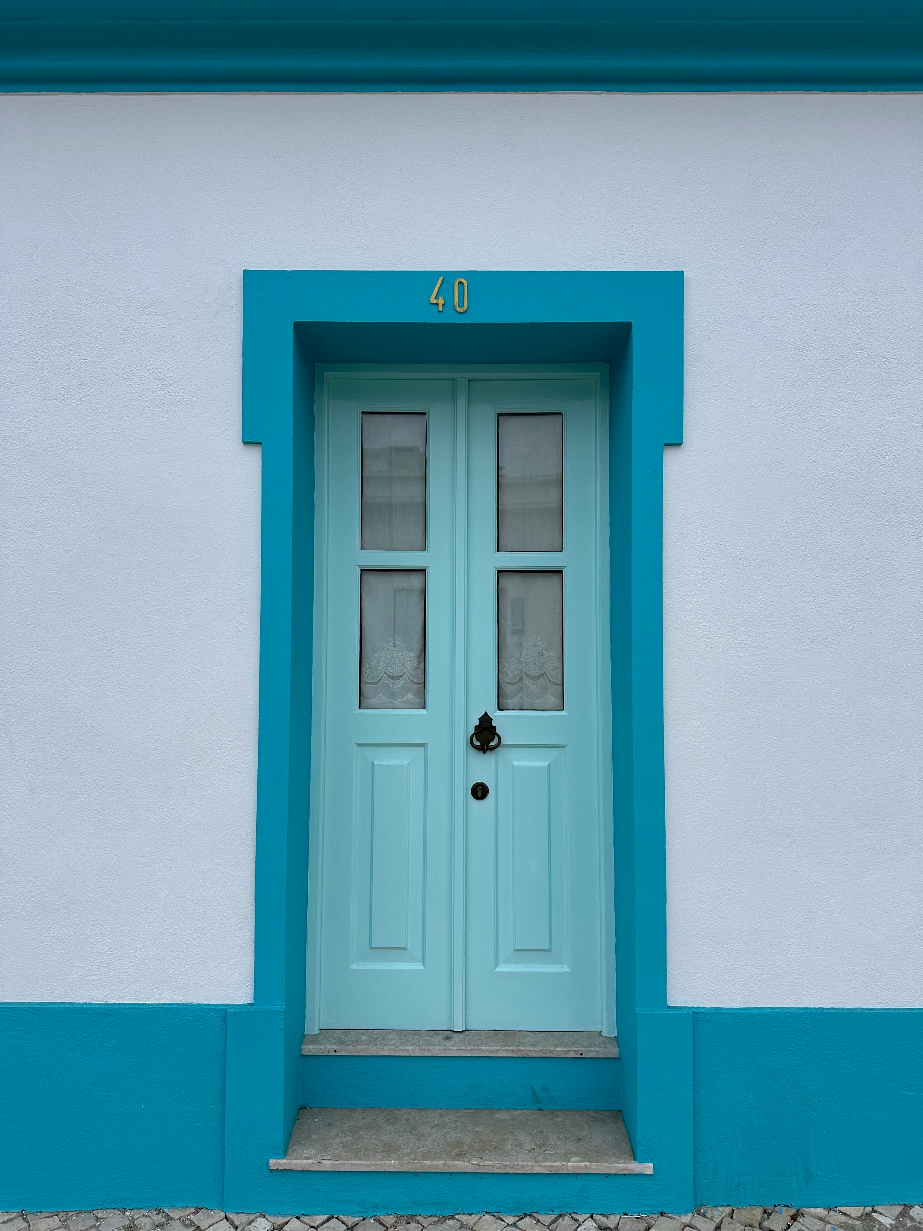 A striking turquoise door framed by a clean facade in Silveira, Lisboa, Portugal.