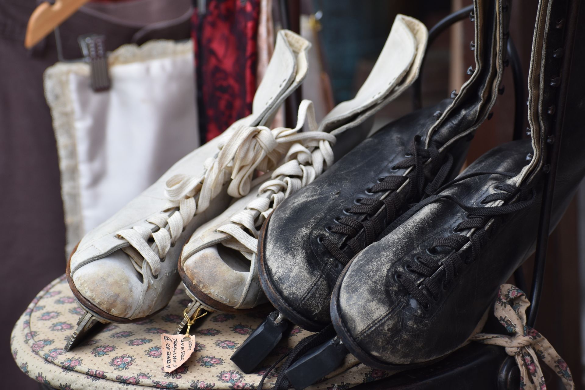 A pair of classic black and white leather figure skates with lace ties on a patterned bench in a vintage store.