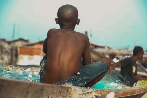 Free A young boy sits on a fishing net, overlooking the sea in Monrovia. Stock Photo