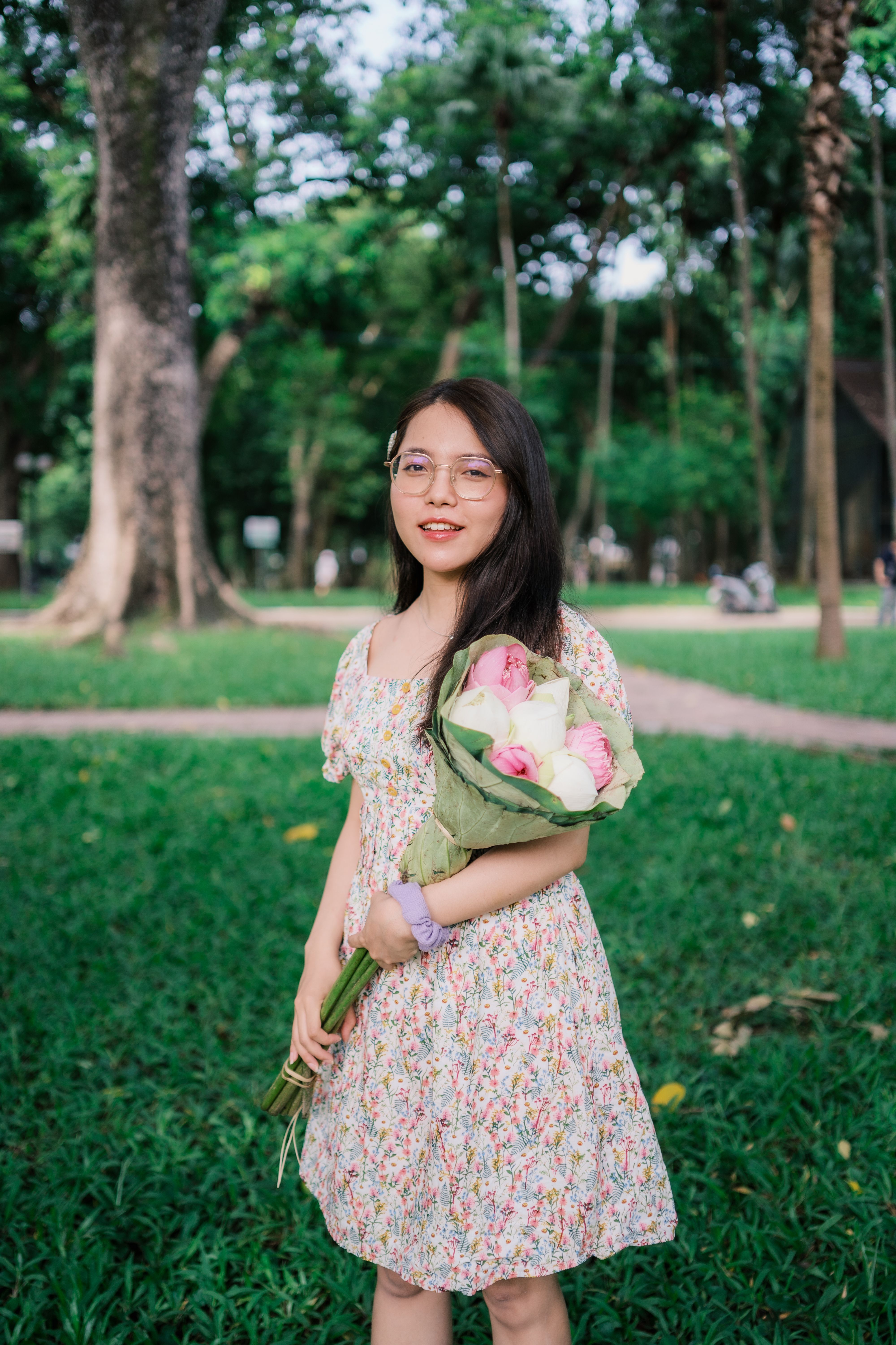A young woman holding flowers in a vibrant park, enjoying a sunny summer day.