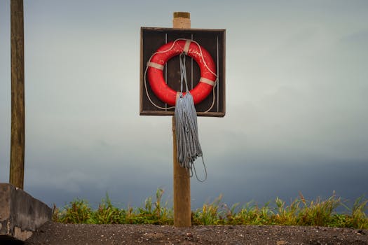 A vibrant red lifebuoy on a post against a moody sky, perfect for coastal safety themes.