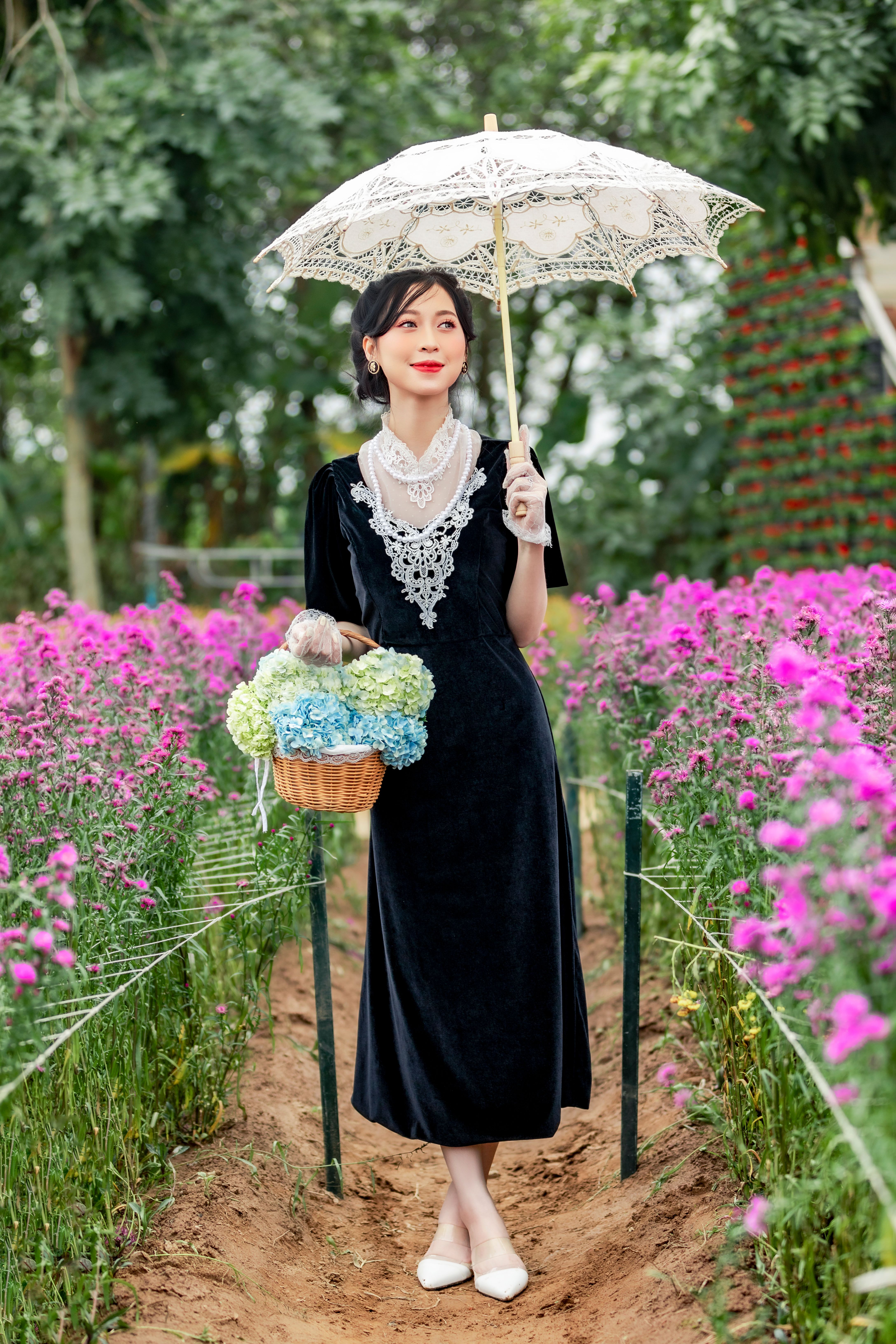 A woman in a black dress holding an umbrella in a flower field  Free Stock  Photo