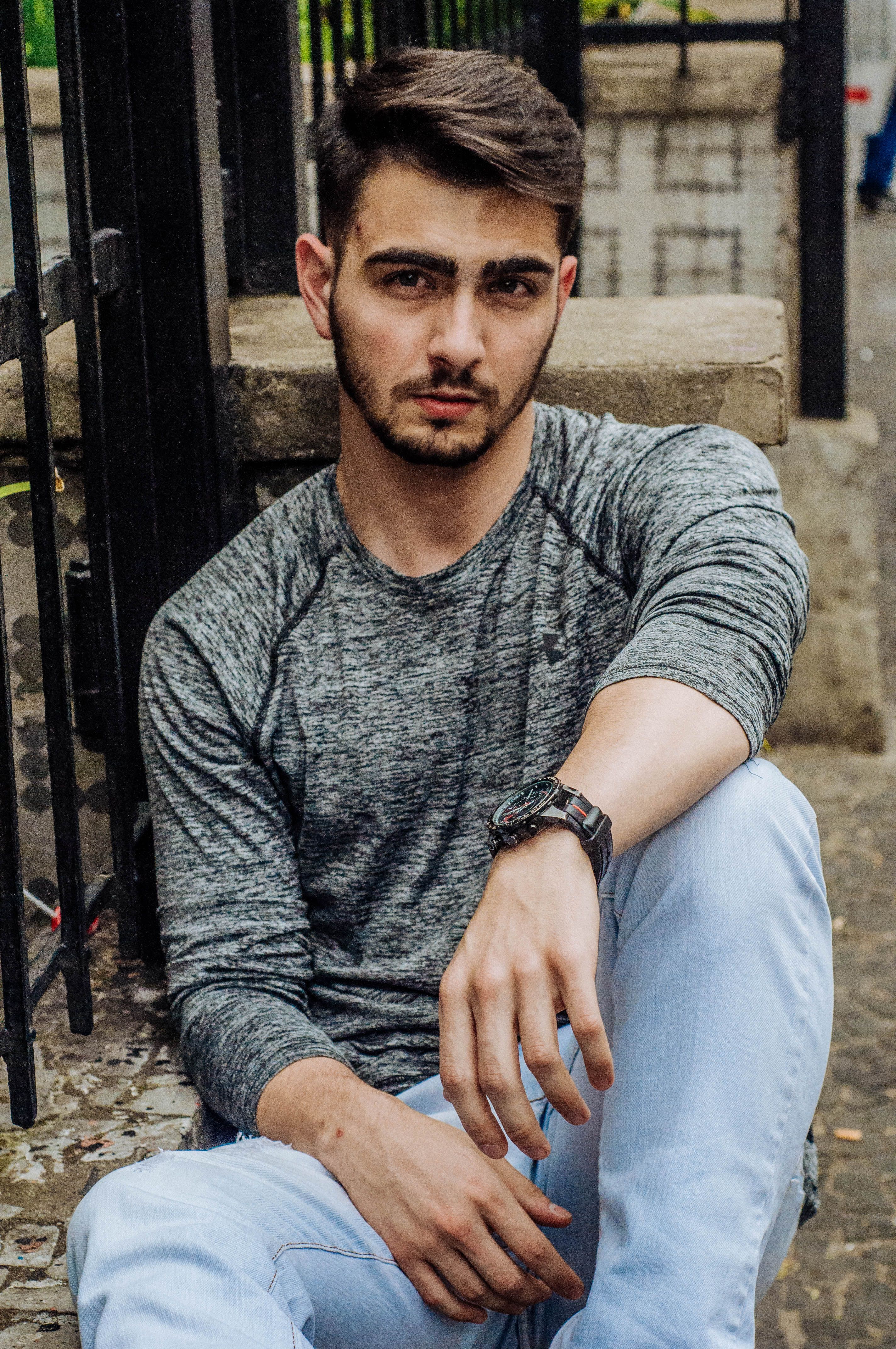 A stylish man in a gray shirt poses in an urban setting, showcasing casual fashion.