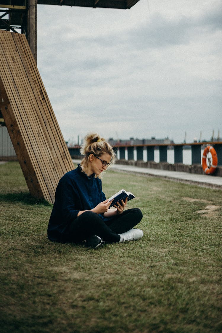 Woman Reading A Book While Sitting In Grass Field