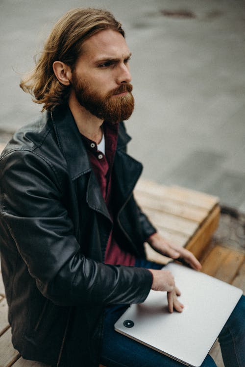 Man Wearing Black Leather Jacket and Holding Silver Laptop