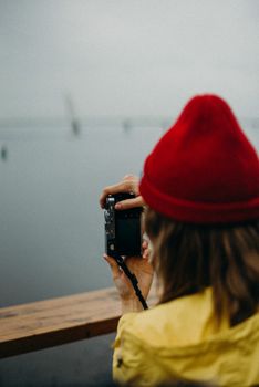Female photographer with a red beanie capturing outdoor scenery with a camera.