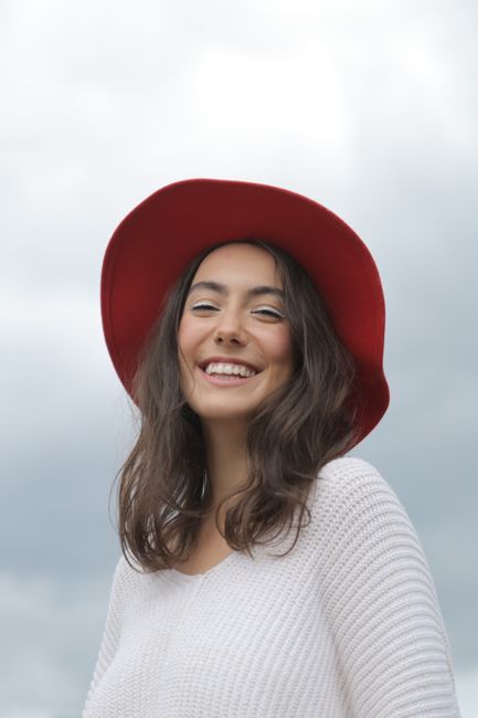 Happy woman in a red hat smiling outdoors in Luss, Scotland, under a cloudy sky.