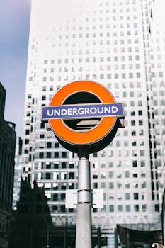 London Underground sign against a modern skyscraper backdrop in Canary Wharf, England.