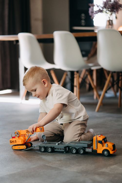 Free A young boy playing with a toy truck on the floor indoors, capturing a moment of playful fun. Stock Photo