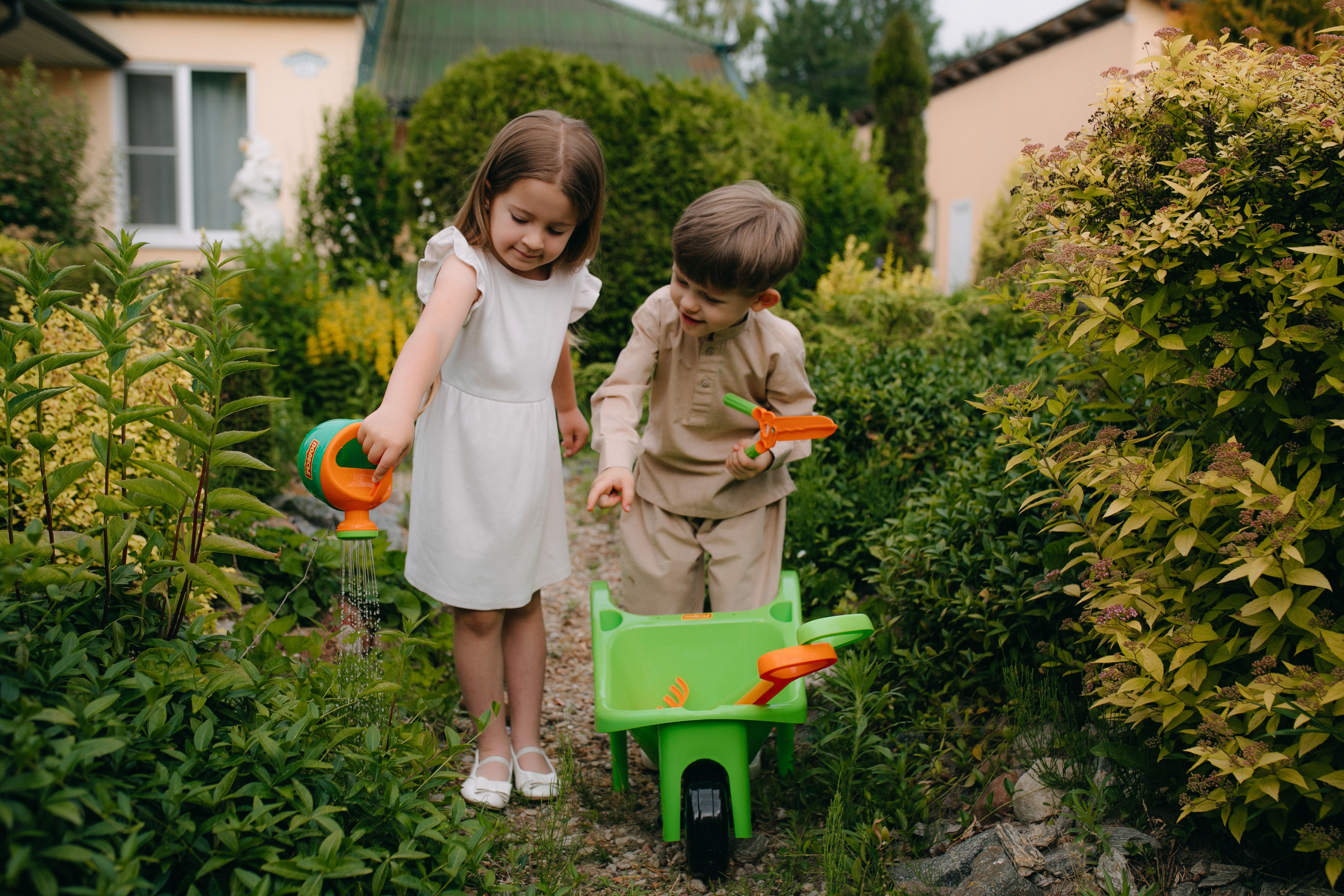 Two children playing in the garden with a wheelbarrow · Free Stock Photo
