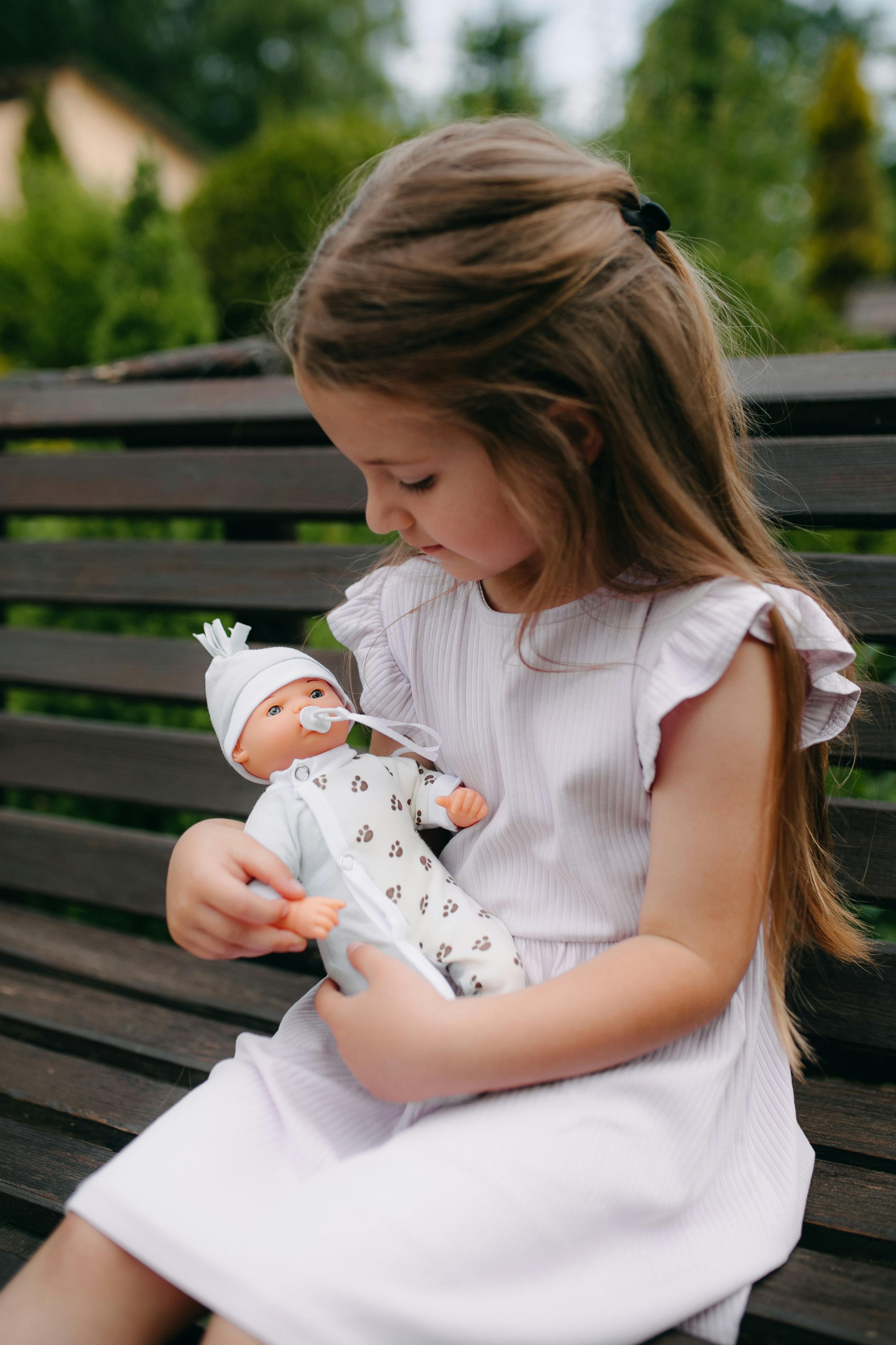 a little girl sitting on a bench holding a doll