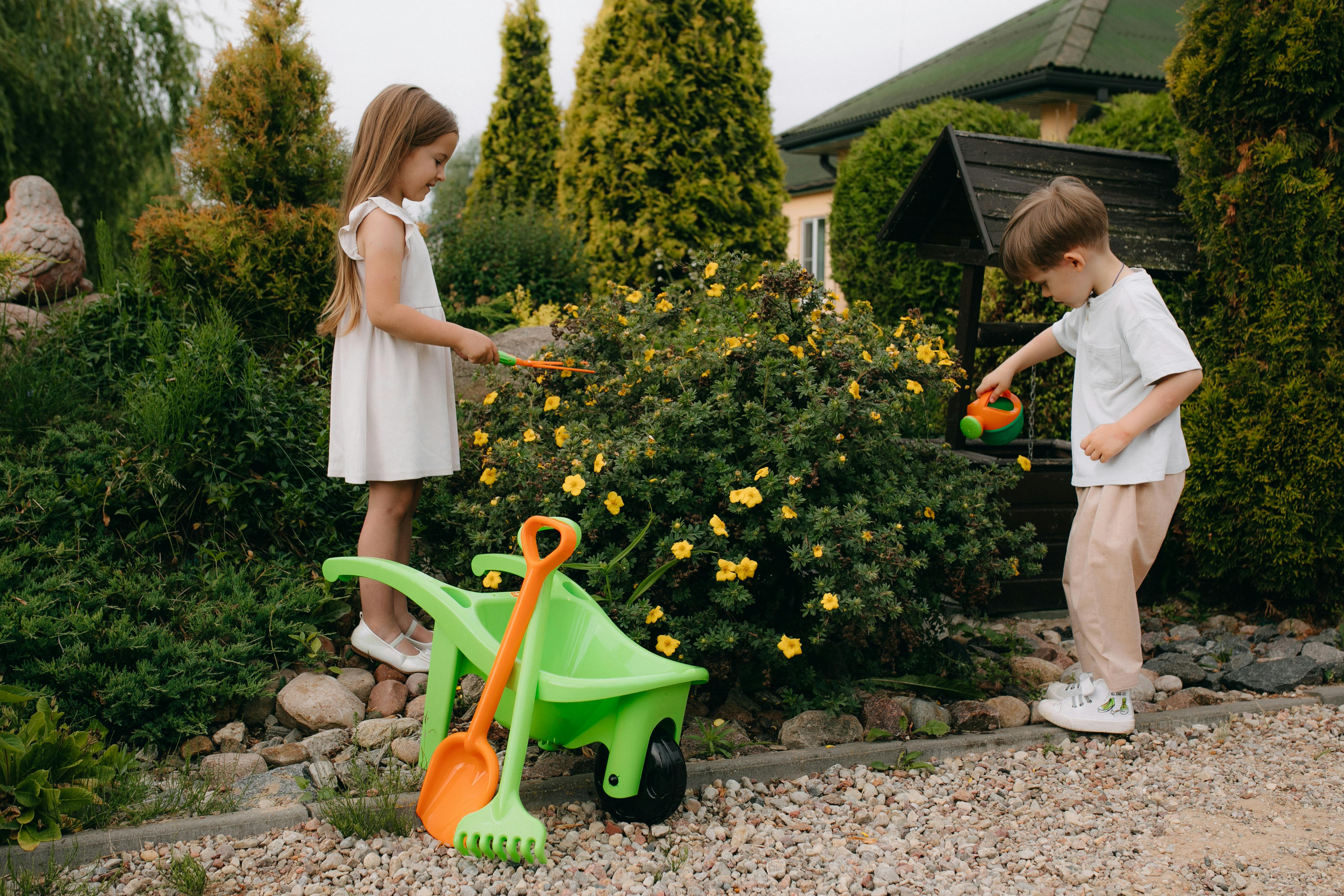 two children playing in the garden with a shovel and wheelbarrow