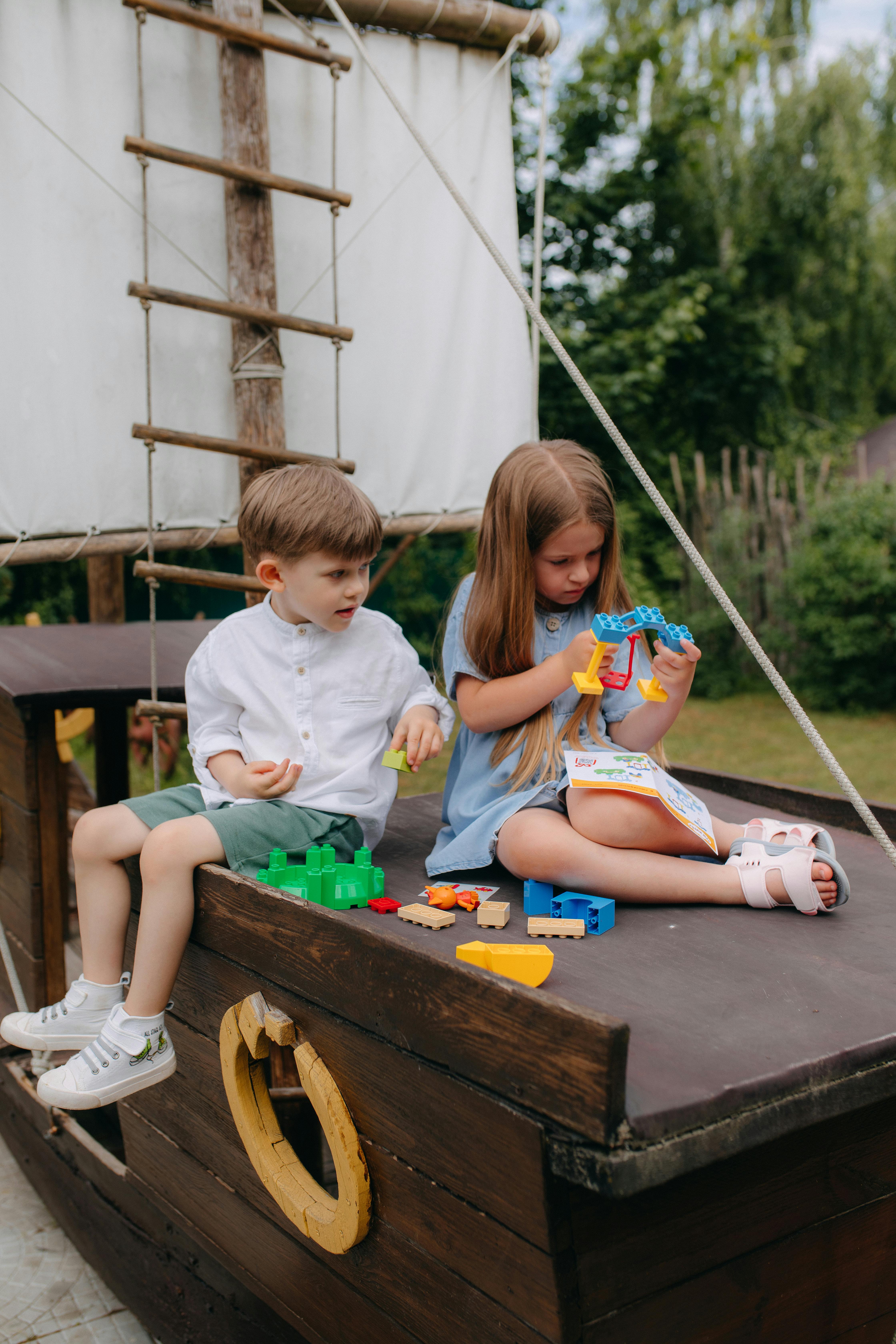 two children sitting on a wooden boat with toys