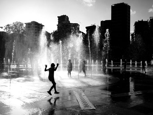 Free Silhouettes play in water fountains against İstanbul's urban skyline. Captured in monochrome. Stock Photo