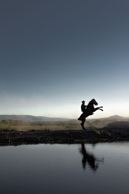 A dramatic silhouette of a horse and rider by a reflective water body against a stunning sunset in Kayseri, Türkiye.