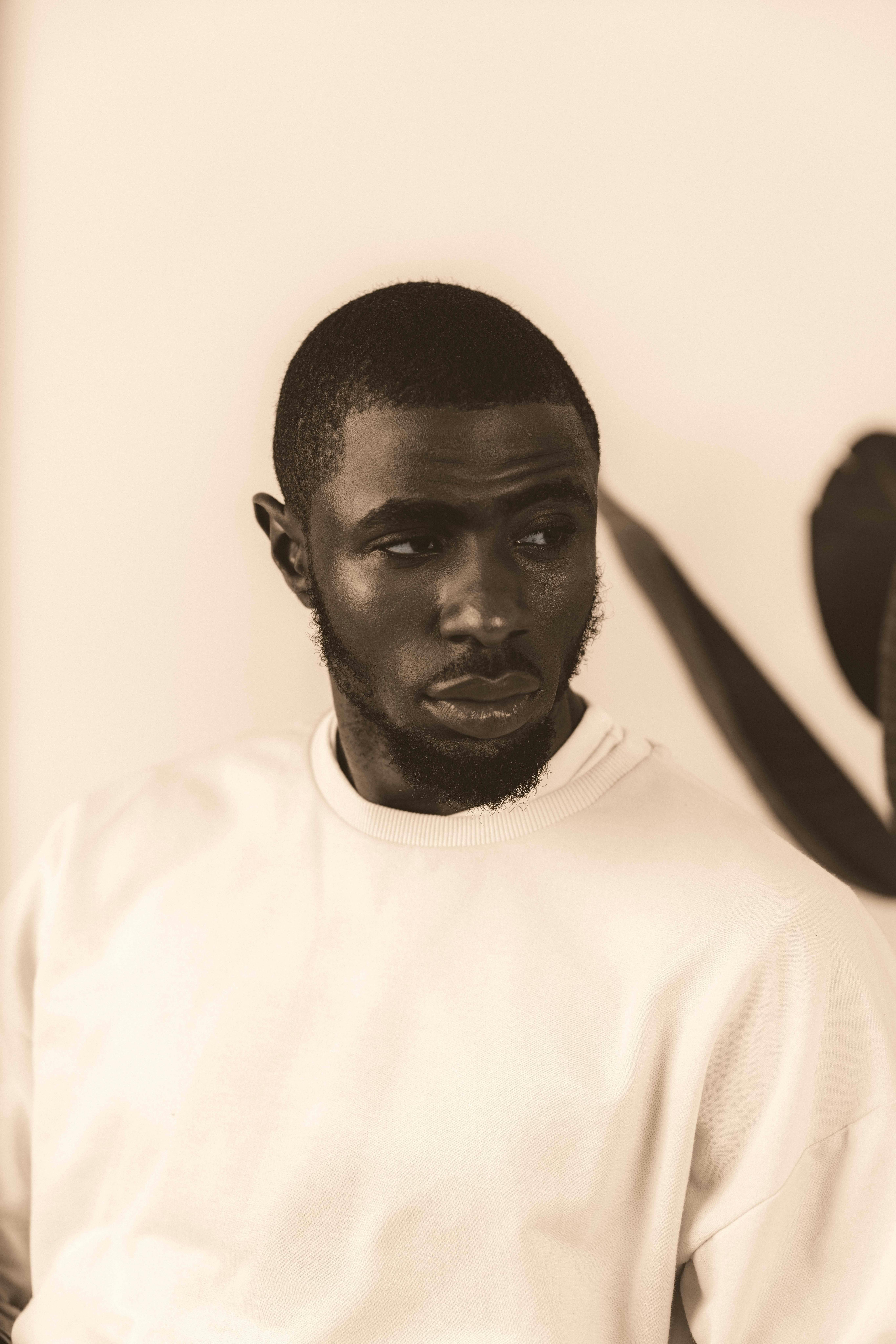 Sepia-toned portrait of a pensive man indoors, showcases fashion and introspection.