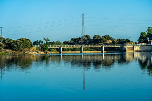 Free Serene view of a bridge over a placid river reflecting the clear blue sky. Stock Photo