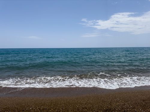 Free Tranquil beachfront scene with gentle waves and clear blue sky, perfect for summer relaxation. Stock Photo