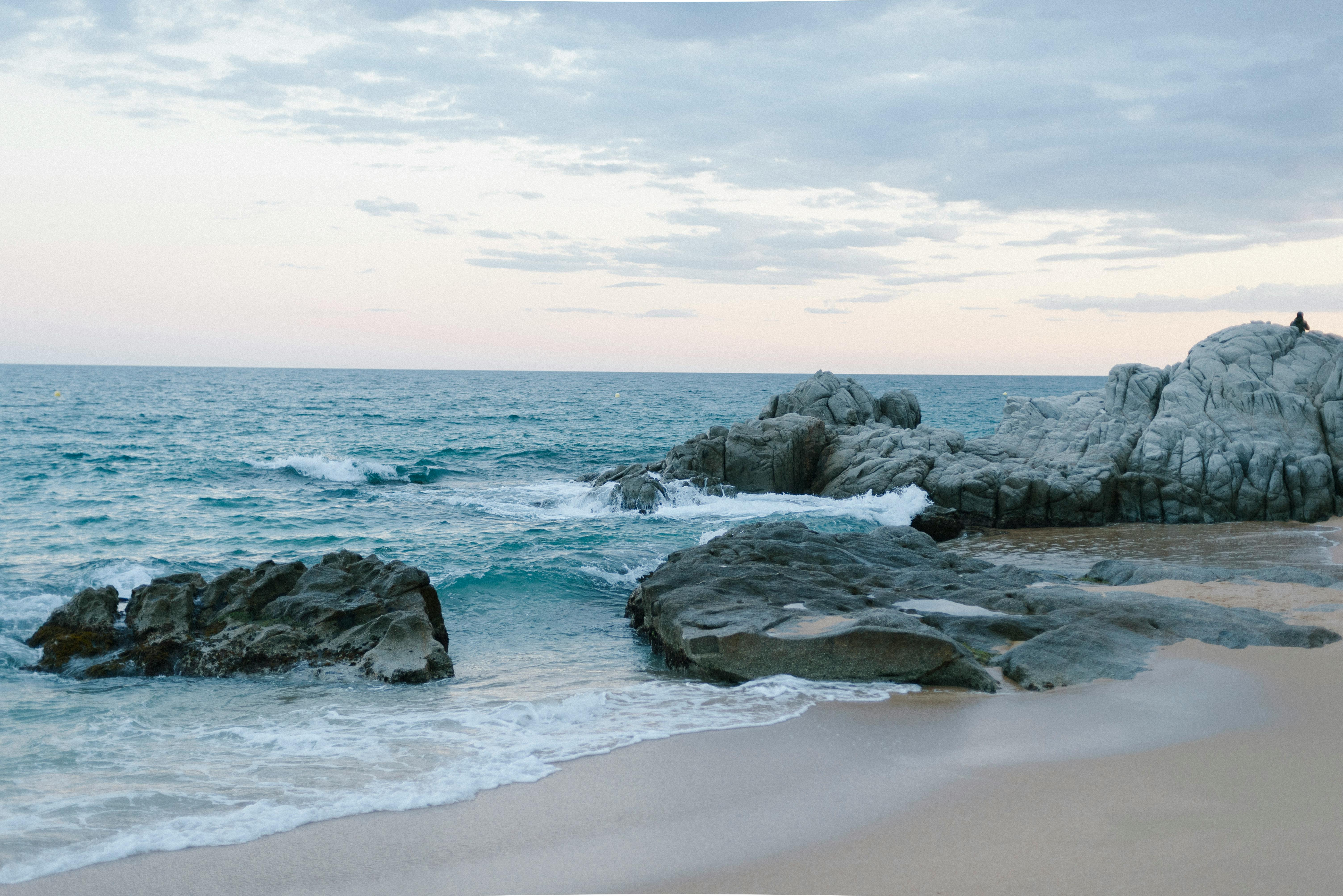 A serene beach with waves crashing against rocks under a pastel sky.